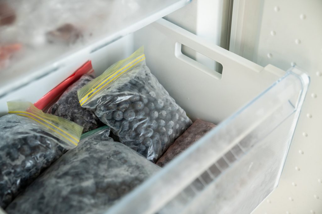 A freezer drawer packed tightly with bags of frozen fruit