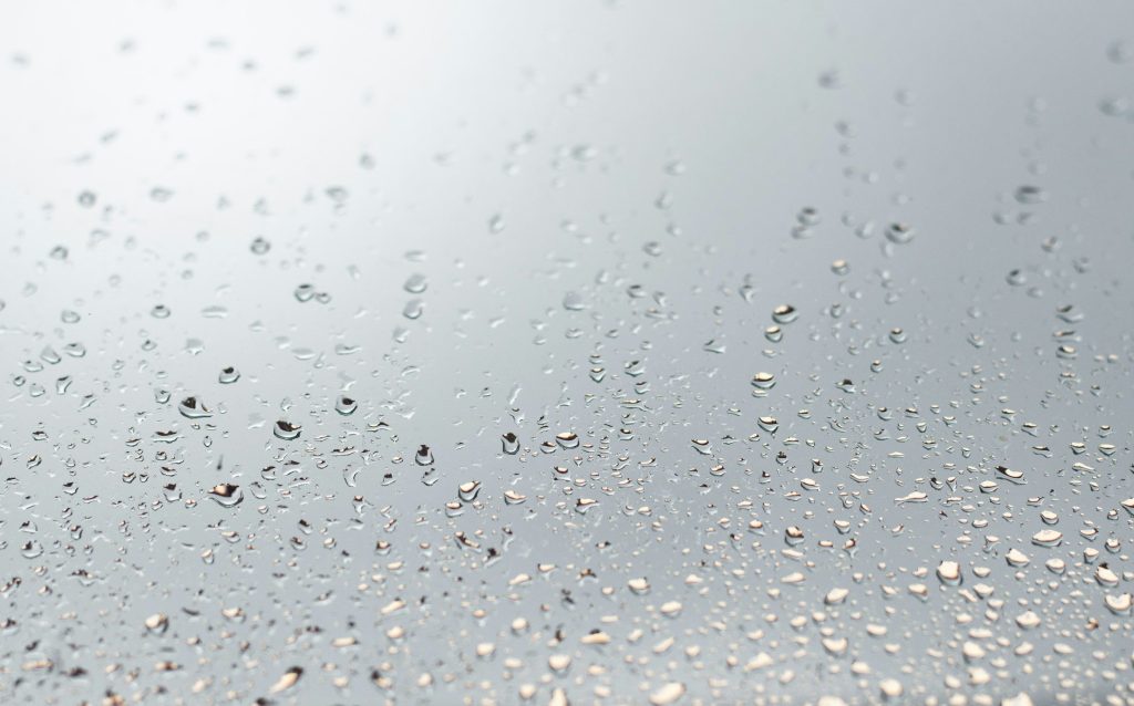 Beads of condensation running down a cold pale surface