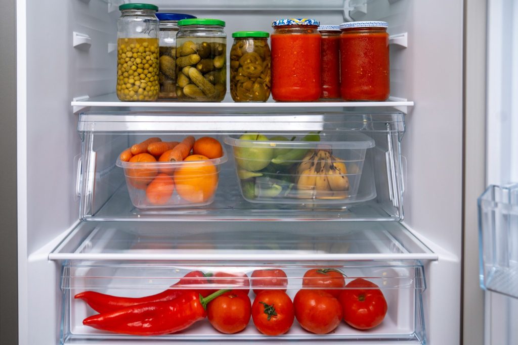Preserving jars above two crisper drawers of tomatoes and peppers
