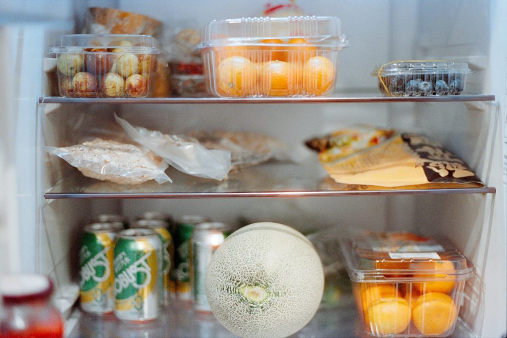 Covered leftovers, a melon and cans on the shelves of a home refrigerator