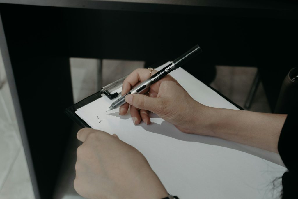 A hand signing a form on a clipboard over a dark glass table