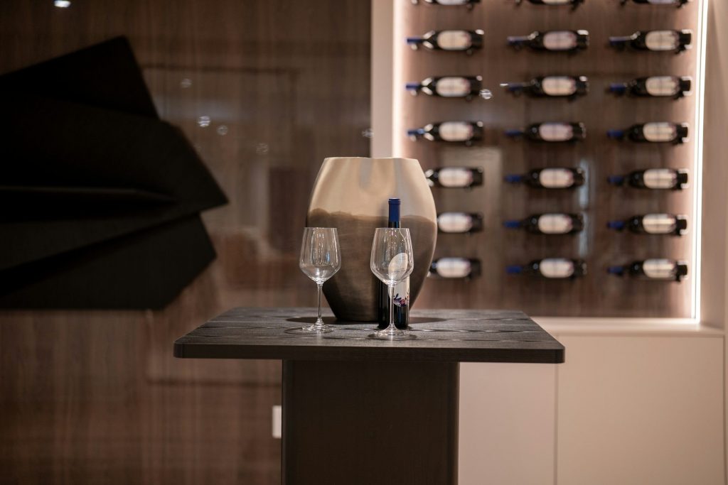 Two glasses and a decanter on a stand in front of a lit wine wall