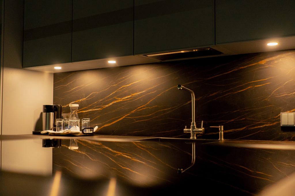 Dark kitchen counter with a gold-veined marble backsplash under warm lighting