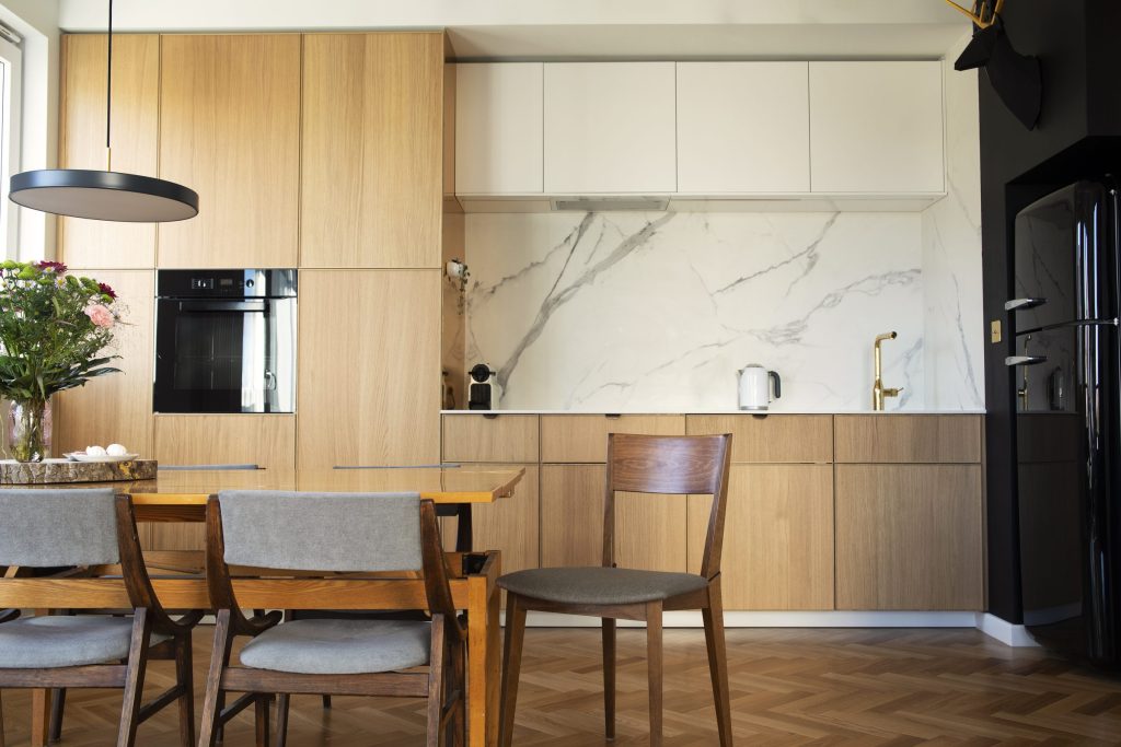 An oak and cream kitchen with a marble splashback and a tall black refrigerator set into the run beside it
