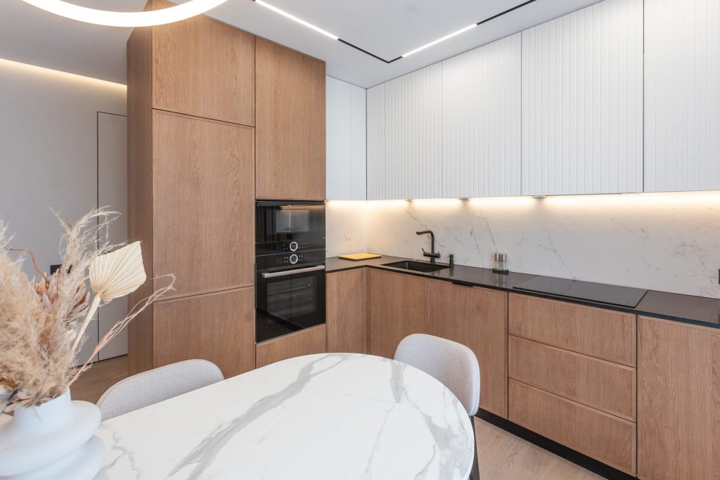 An oak and white handleless kitchen with a stacked oven column and a marble dining table in front