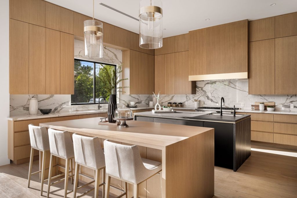 An oak kitchen with a long island and stools, a marble splashback and a dark cooking run behind