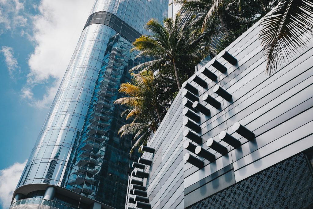 A glass office tower and a fluted white facade with a palm between them