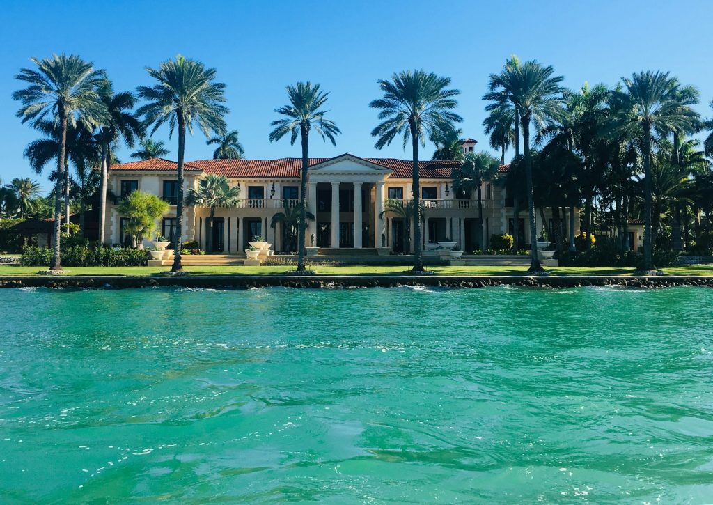 A columned waterfront house behind coconut palms, seen from the water