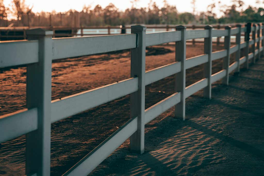 A white equestrian fence around a sand riding arena at sunset