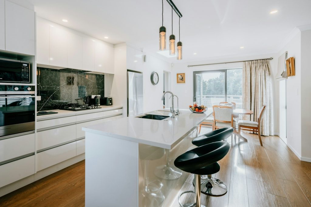 A white kitchen with a green stone splashback and three black stools
