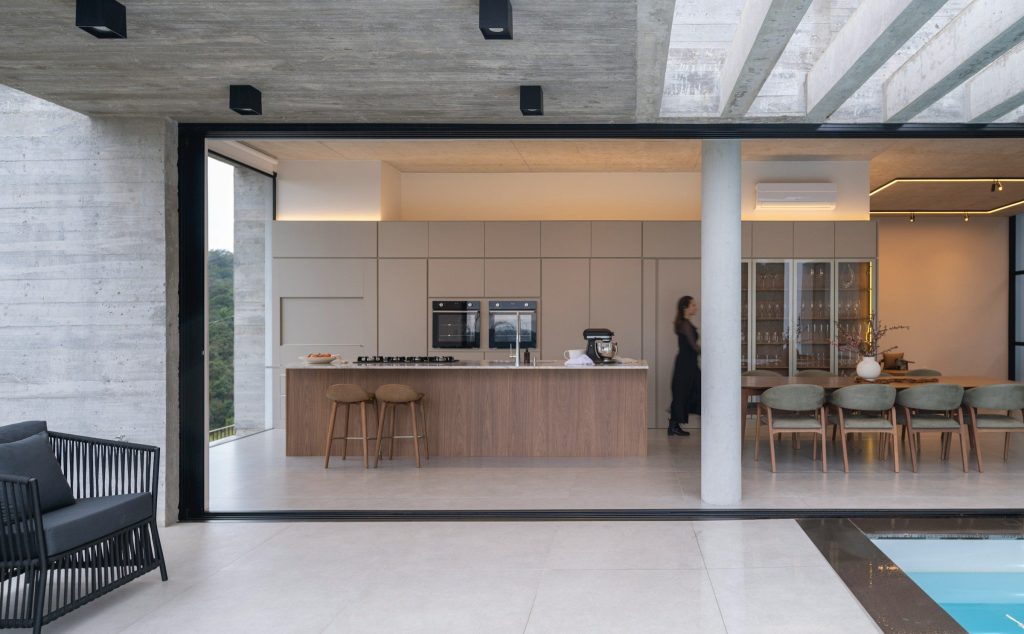 A kitchen open to a terrace and a pool beyond, seen from outside