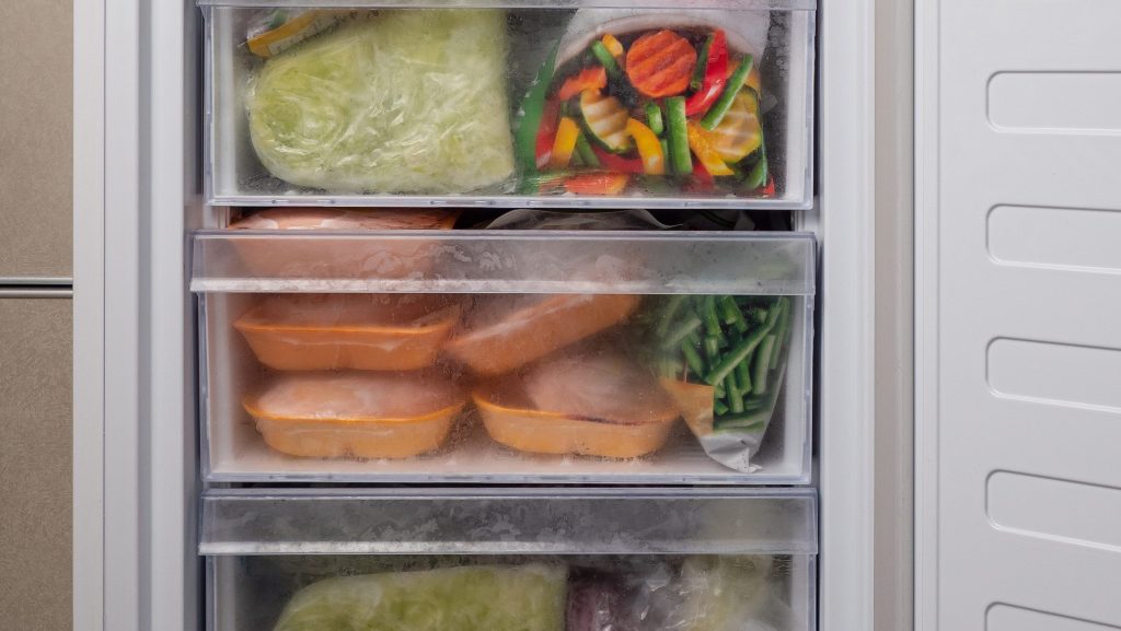 An open freezer drawer packed with bags of frozen vegetables