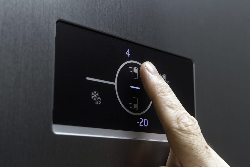 A finger pressing a refrigerator touch panel showing the fridge and freezer set temperatures