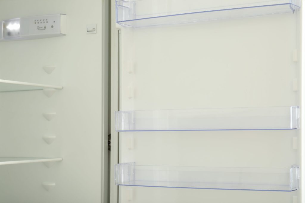 An empty refrigerator interior with bare glass shelves and door racks