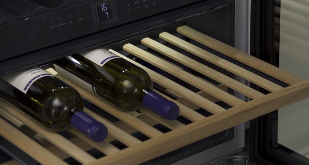 An open wine cabinet drawer with two bottles on wooden slats, the control panel above showing the set temperature